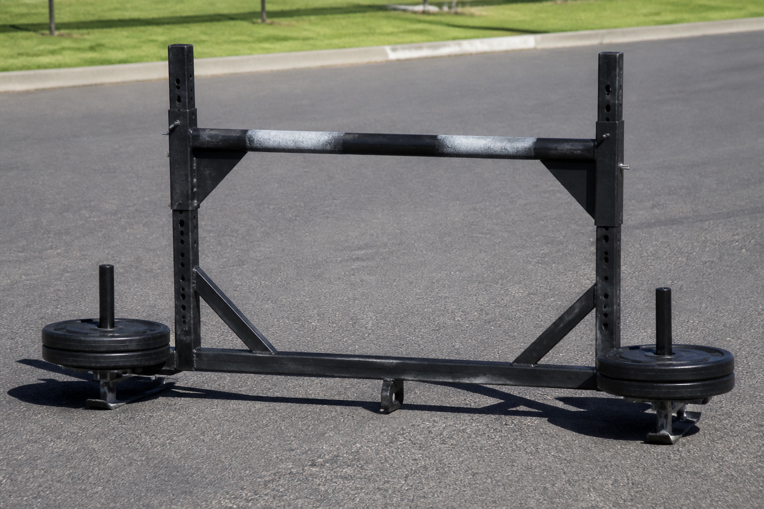 A heavy metal yoke used in strongman competitions standing on an asphalt track, professional sports photography style, bright daylight.