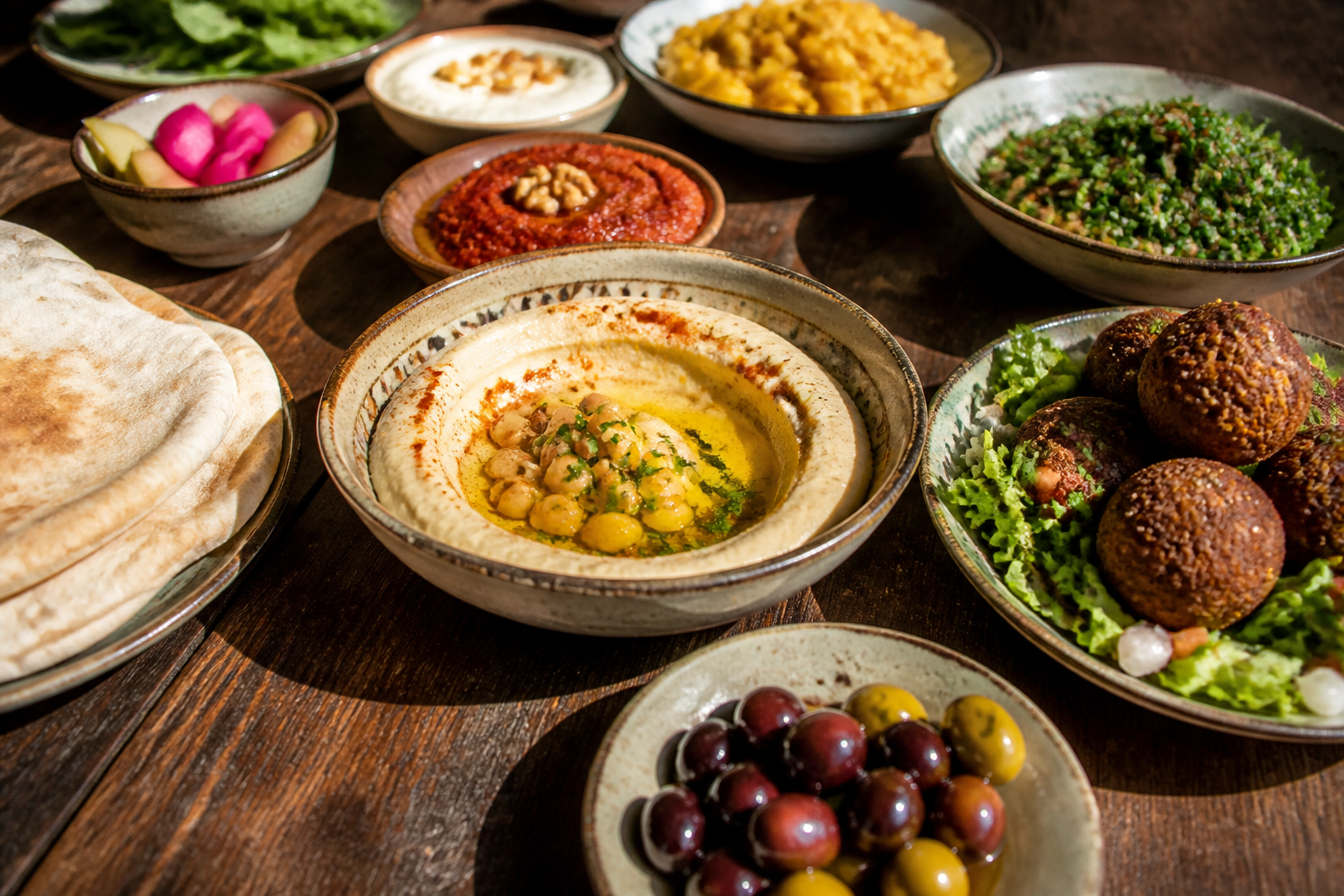 A vibrant Lebanese mezze spread with hummus, falafel, pita bread, and olives on a rustic wooden table, warm sunlight.