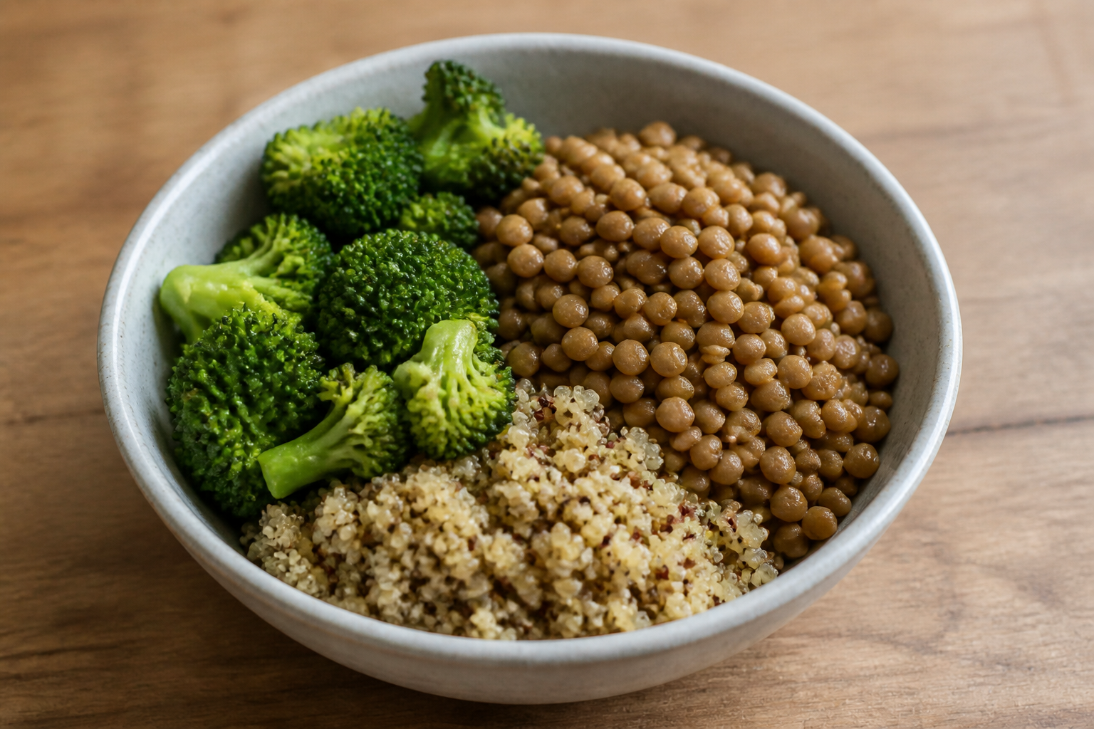 A high-angle shot of a ceramic bowl filled with cooked lentils, quinoa, and vibrant green broccoli, natural soft window lighting.