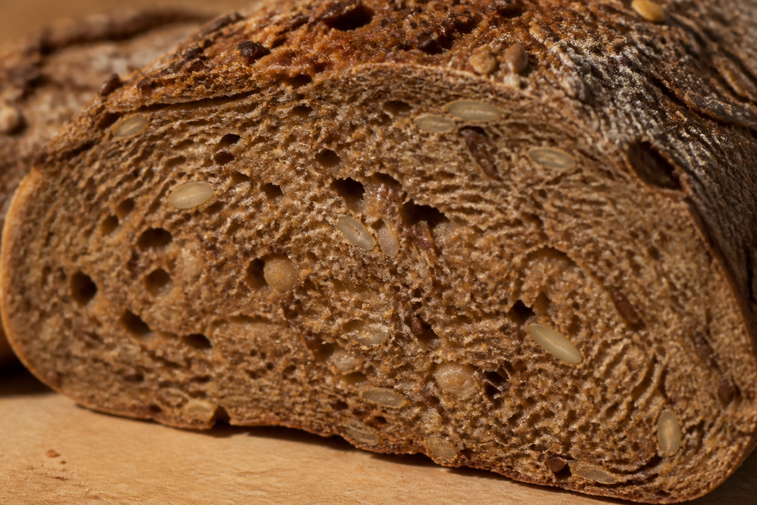 Macro photograph of a sliced loaf of dense whole grain rye bread, showing intricate seeds, grains, and fiber textures, warm soft lighting.