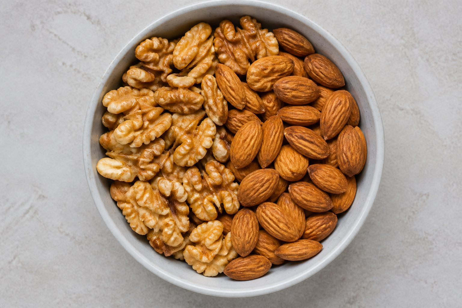 A top-down view of a ceramic bowl filled with raw walnuts and almonds, clean minimalist background, sharp focus on nut textures.